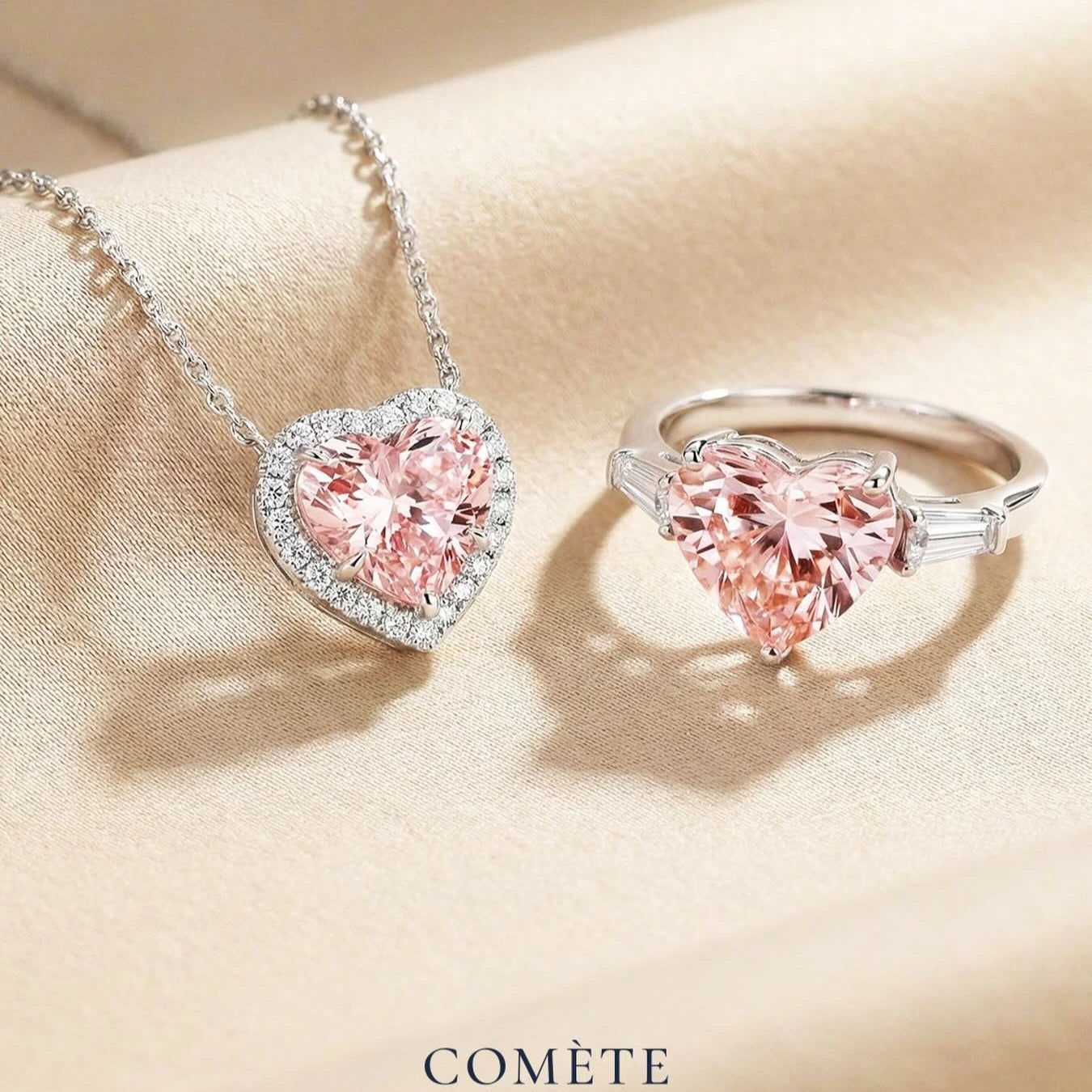 Heart-shaped pink gemstone necklace and ring on a beige fabric background with 'COMèTE' branding.