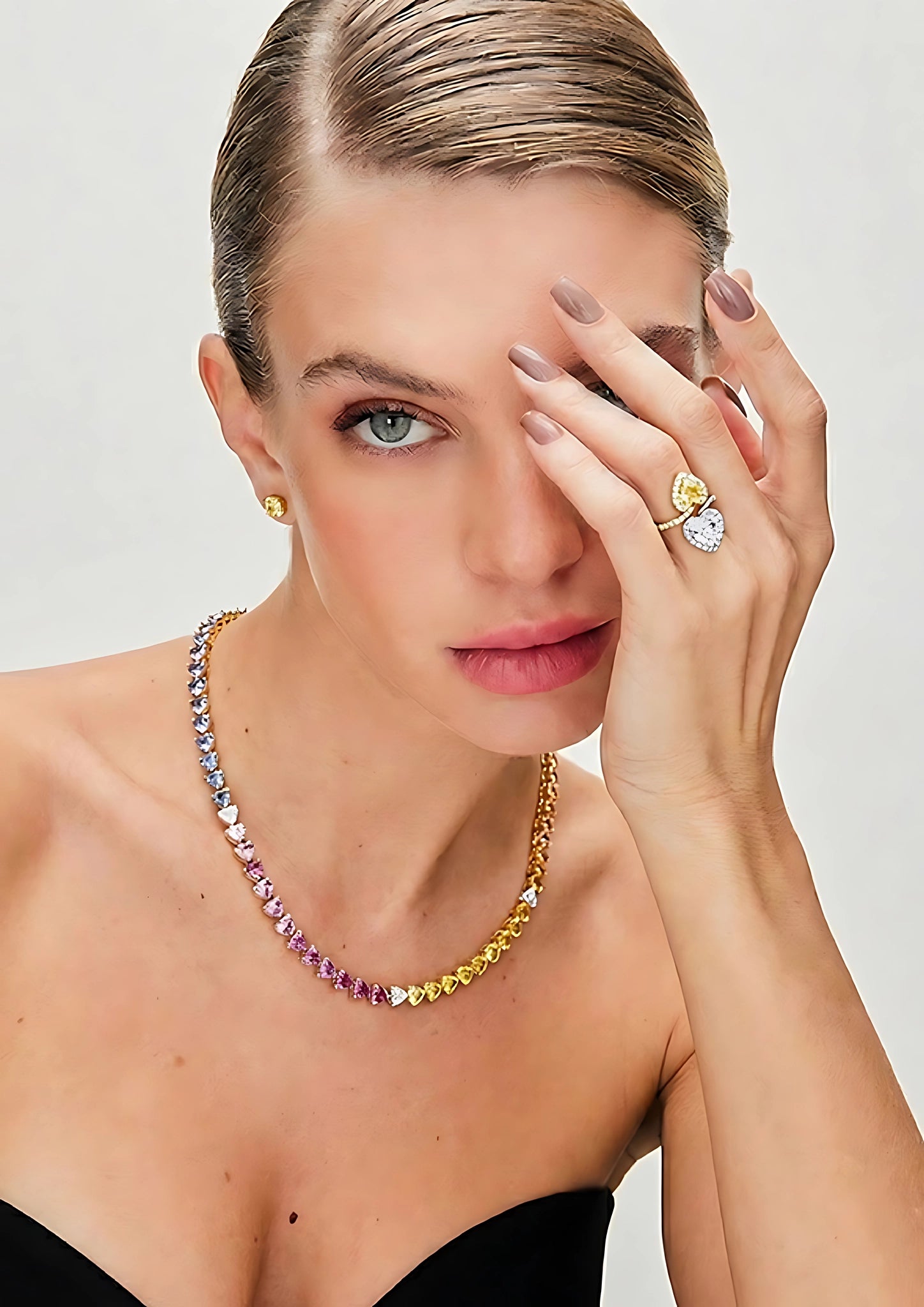 Woman wearing a colorful gemstone necklace, earrings, and ring on a plain background